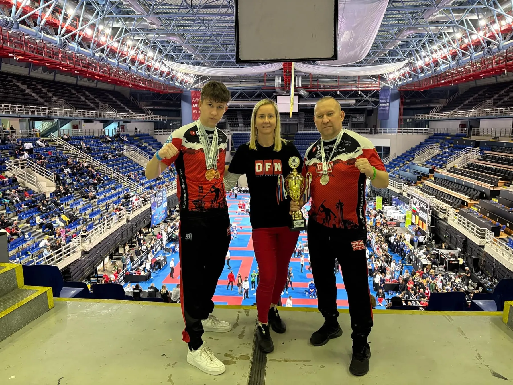 Oskar, Agnieszka i Tomasz Biernaccy z pucharem i medalami na tle areny w Atenach